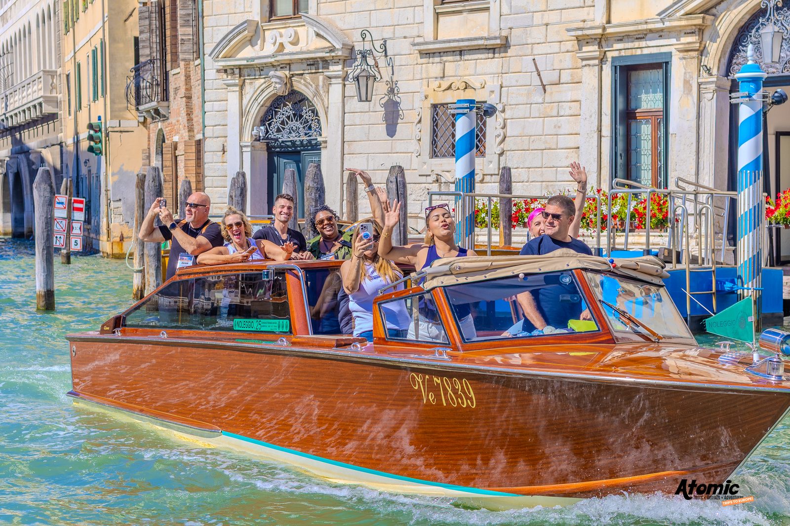 An Atomic Trips group waving from a boat on a Venice canal