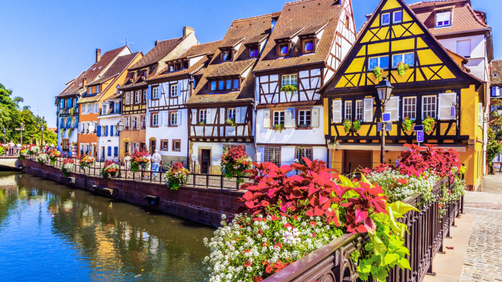 a row of colorful buildings with flowers and a bridge over water
